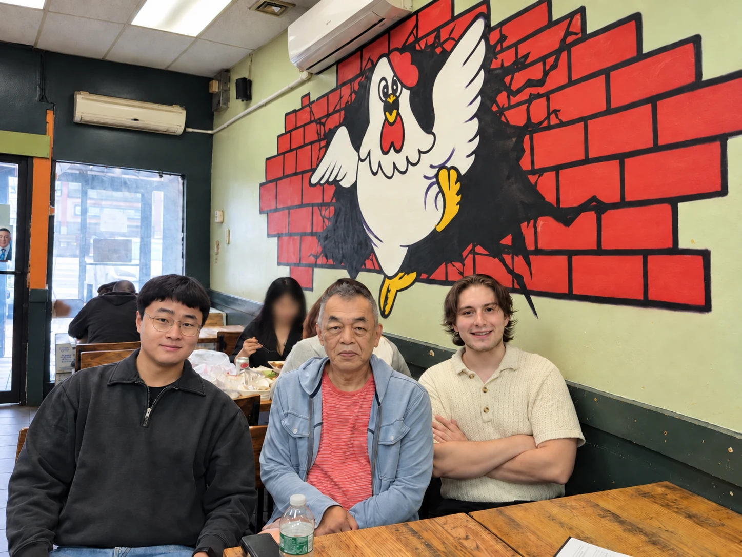 Robert from Chicken Lovers sitting with two Inyeon team members beneath the restaurant’s chicken mural.